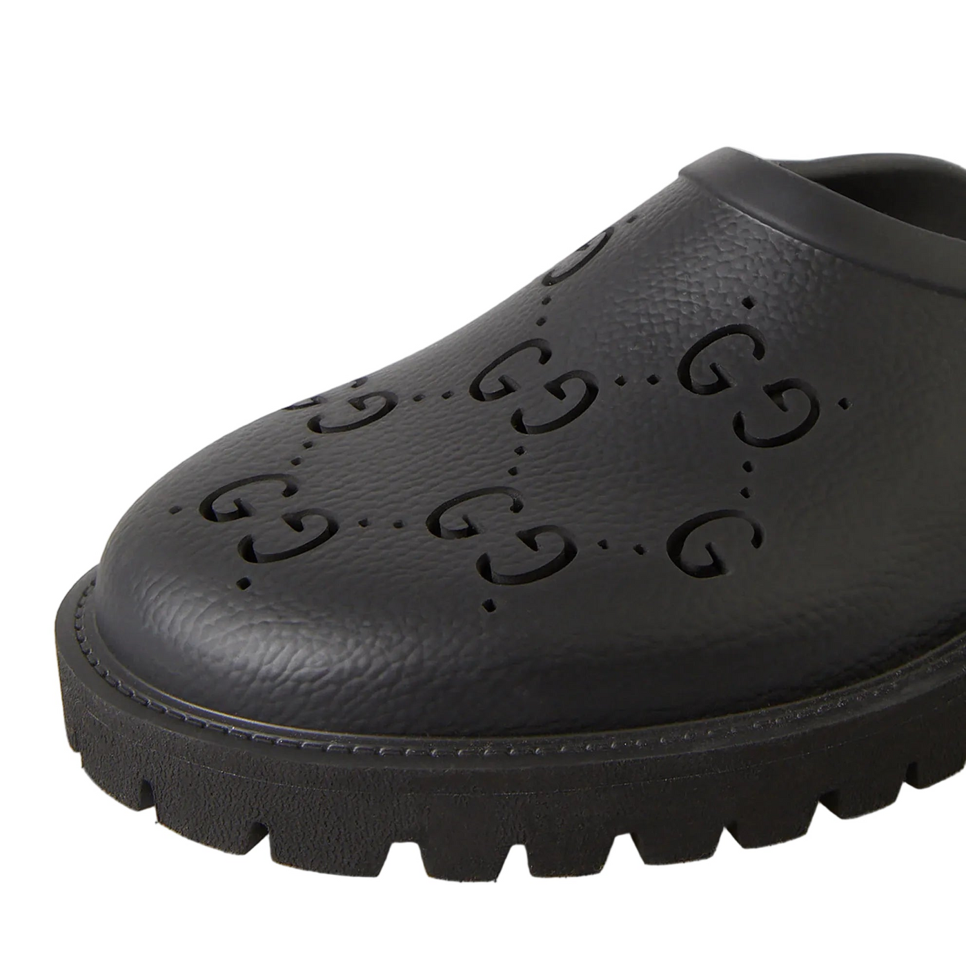A close-up of a black Gucci clog shoe featuring embossed GG monogram patterns on the toe and a chunky lug sole, set against a light gray background.